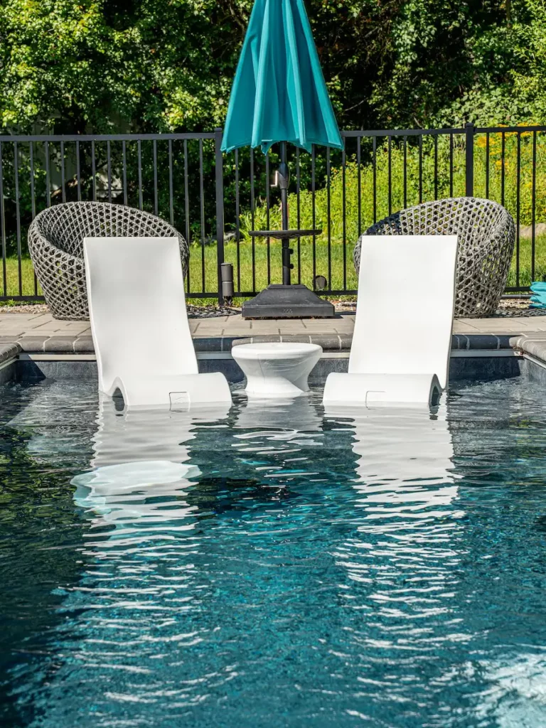 Two white lounge chairs and a table set in the sun-shelf of a Plunge Pool Concepts pool.