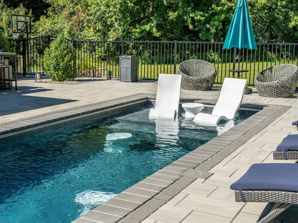 Two white lounge chairs and a table set in the sun-shelf of a backyard pool.