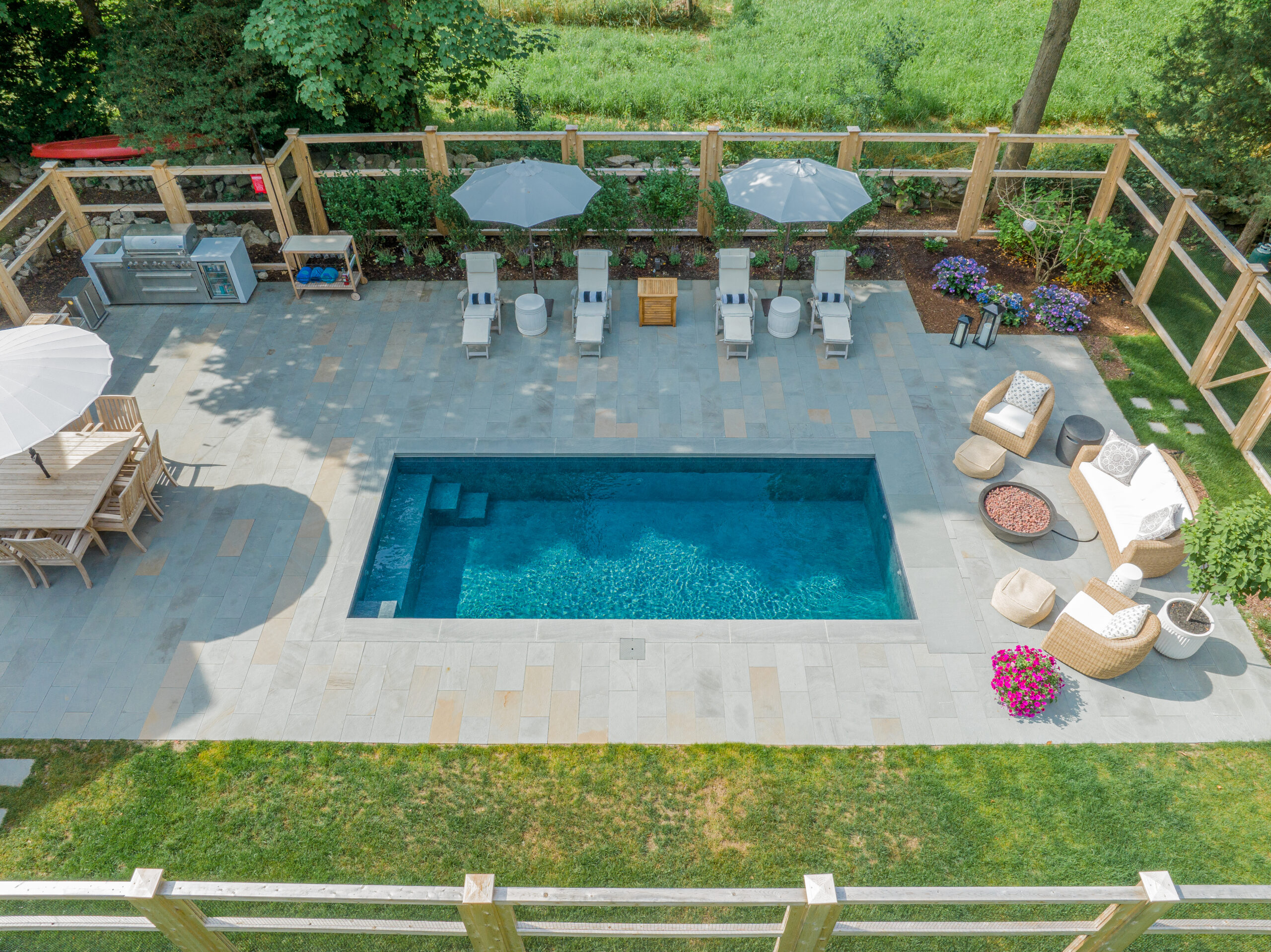 Backyard plunge pool with blue water, slate pavers, three chaise lounges under umbrellas, dining area, and fire-pit seating.