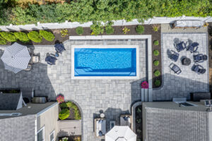 9'x20' Quantum Composite Plunge Pool with Horizon interior and stone coping, surrounded by gray stone pavers and backyard seating area.