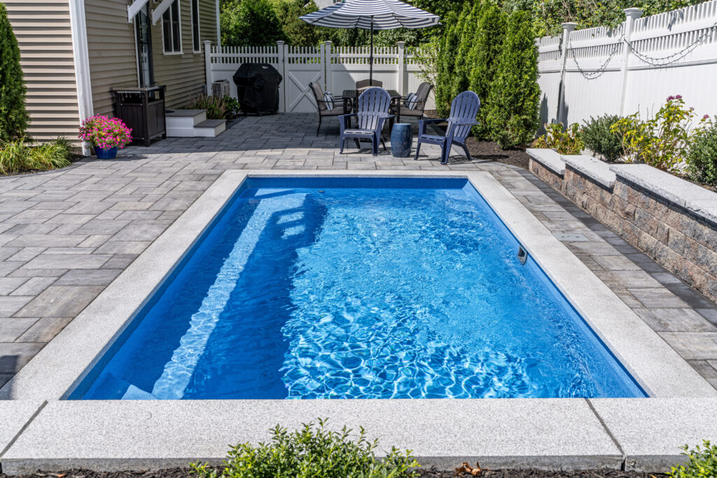 9'x20' Quantum Composite Plunge Pool with Horizon interior and stone coping, surrounded by gray stone pavers and backyard seating area.